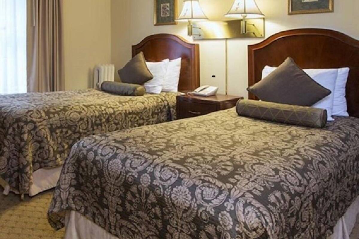 A hotel room with two beds, each with a patterned bedspread, a nightstand with a lamp, and a framed picture on the wall.