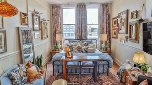A cozy room with a bed, a desk, and a sofa. There are curtains, a ceiling fan, and framed pictures on the walls. - Walk Everywhere - Charming Studio on the Riverwalk (San Antonio)