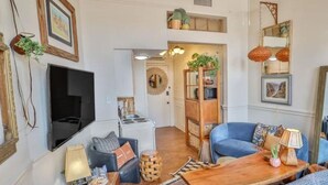 A living room with a TV, sofa, coffee table, and decorative items. - Walk Everywhere - Charming Studio on the Riverwalk (San Antonio)