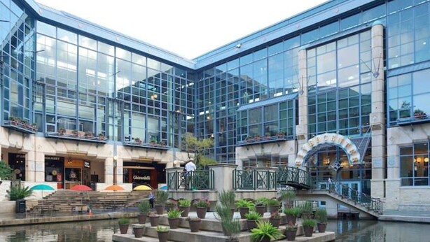 A modern building with large glass windows, a central courtyard with a water feature, and a staircase leading to an upper level. - Walk Everywhere - Charming Studio on the Riverwalk (San Antonio)