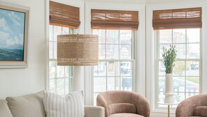Ett vardagsrum med en beige soffa, två fåtöljer, ett runt soffbord i trä och en golvlampa.