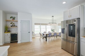 A modern kitchen with white cabinets, a stainless steel refrigerator, and a dining area with a table and chairs. - Beach Block • Sleeps 16 • Free Parking • Perfect for Groups (Atlantic City)