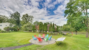 Un espace extérieur verdoyant, aménagé avec des sièges disposés en cercle, comprenant des fauteuils Adirondack aux couleurs vives et une petite table.