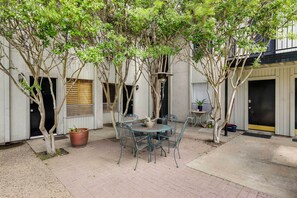 Eine Terrasse mit rundem Tisch und Stühlen, umgeben von Bäumen und einem Gebäude mit weißer Fassade und Holzhörnern.