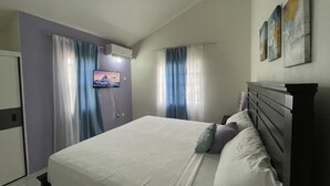 Una camera da letto con un letto, tende, una TV a muro e opere d'arte appese.
