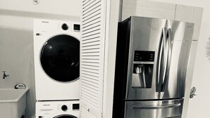 Una cucina compatta con frigorifero in acciaio inossidabile, lavatrice e asciugatrice affiancate e un piccolo lavello.