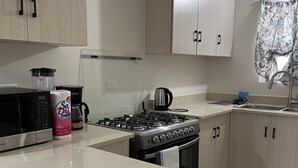 Una cucina moderna con piano cottura in acciaio inossidabile, un forno a microonde e una macchina da caffè. Presenti inoltre mobili in legno e una parete rivestita in piastrelle.