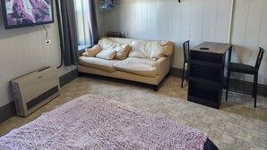 Une pièce avec un canapé beige, une petite table, une chaise, un téléviseur fixé au mur et un radiateur.