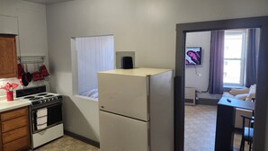 Une cuisine compacte équipée d’une cuisinière, d’un four et d’un réfrigérateur, d’une fenêtre avec des rideaux et d’un petit coin salon avec un téléviseur.