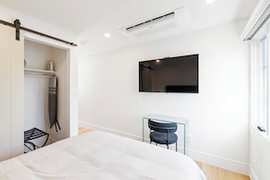 Quarto moderno com cama, escrivaninha e TV fixada na parede.