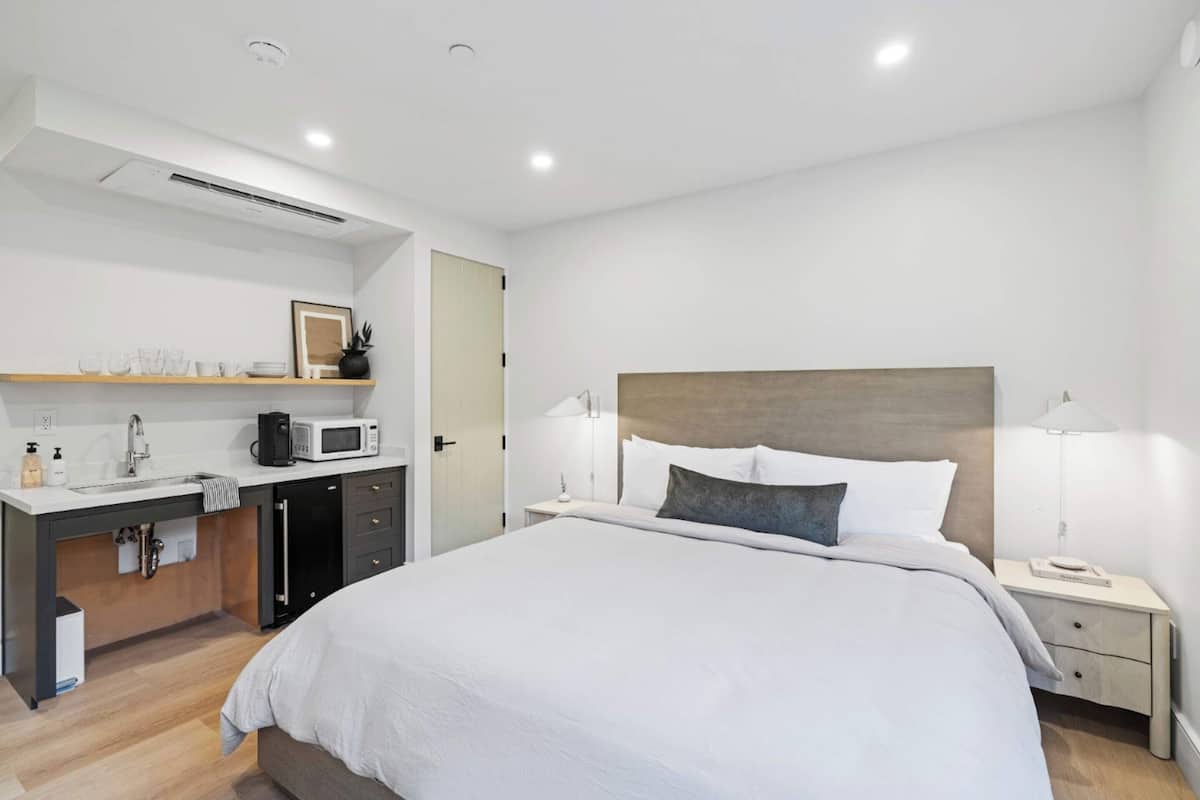 Relax in a spacious room with a large bed, bedside table, and desk area featuring a microwave and coffee maker.