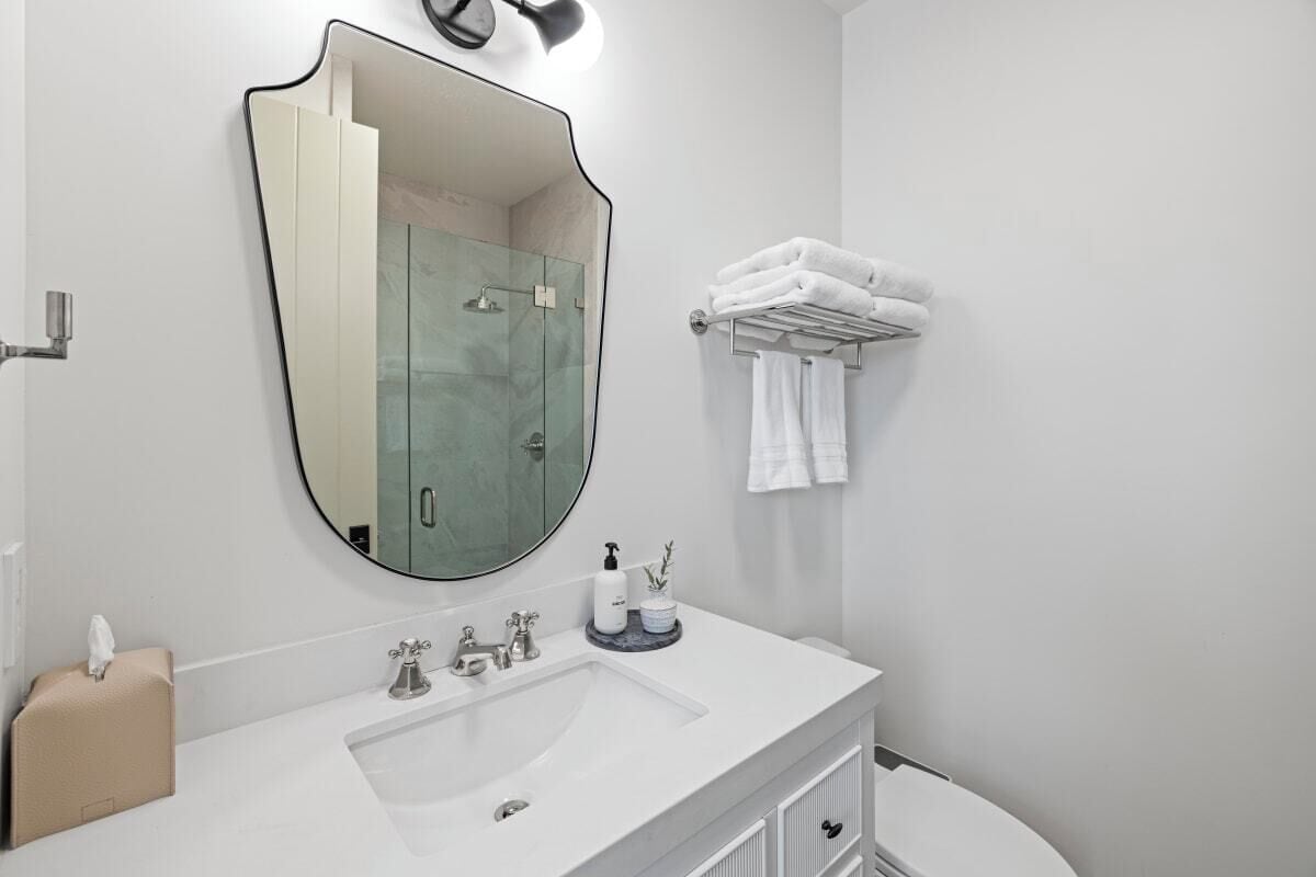 A modern bathroom with a large mirror, a sink, and a toilet.