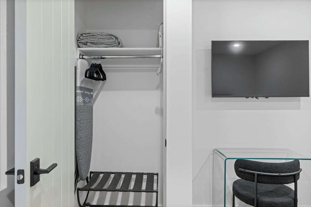 A modern bathroom with a towel rack, a shower area, a glass-enclosed chair, and a mounted TV.