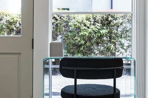 A chair with a textured seat and backrest, positioned in front of a window with a view of greenery outside. - Casa Jardin (Santa Barbara)