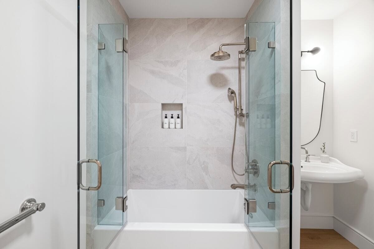 A modern bathroom with a glass-enclosed shower, a white bathtub, and a white sink.