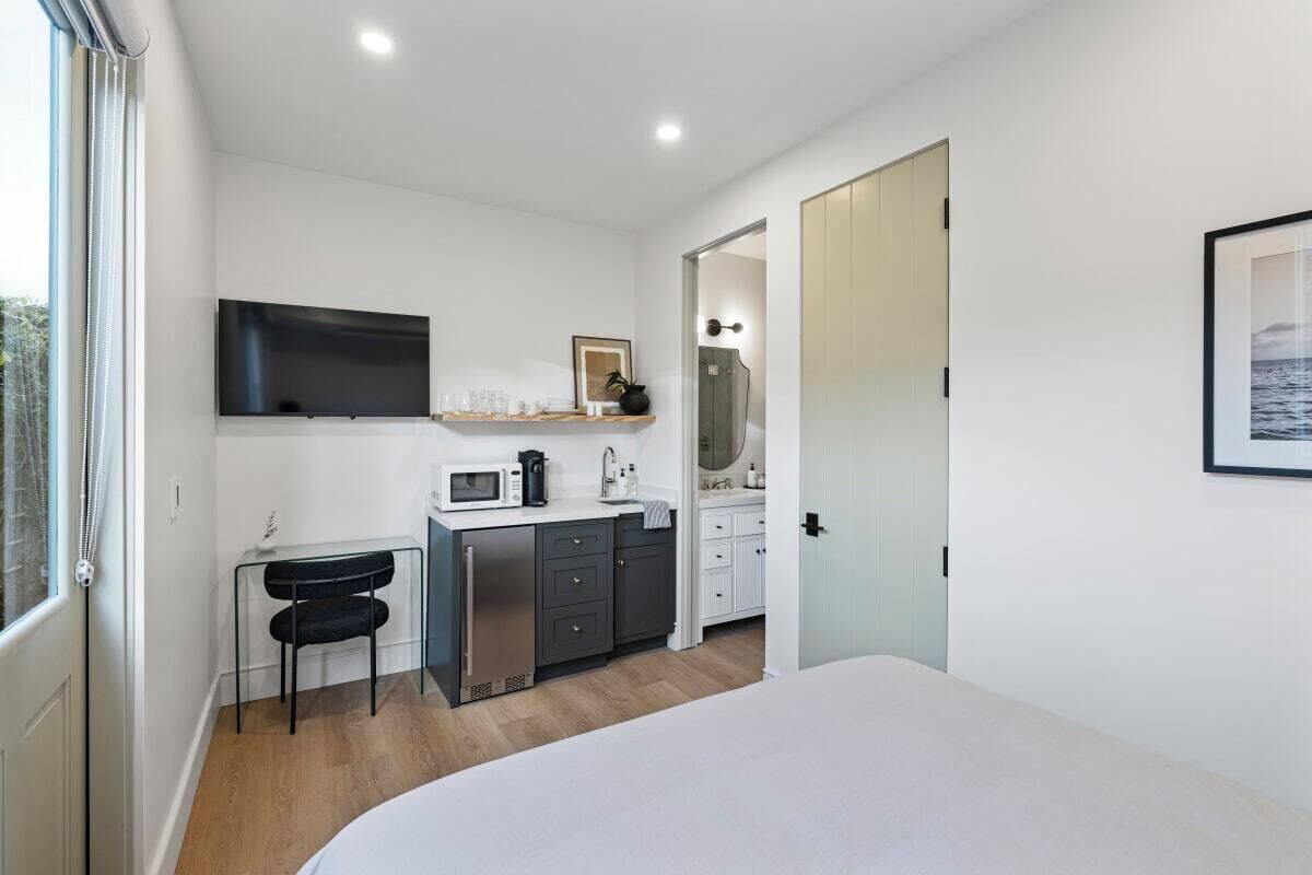 A modern bedroom with a bed, a desk with a chair, a microwave, and a small kitchenette.