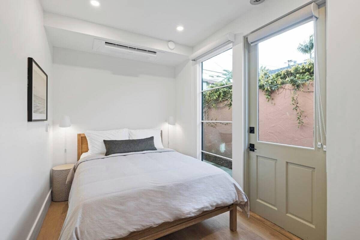 A bedroom with a bed, bedside lamps, a small bedside table, and a door leading to an outdoor area.