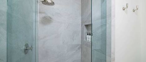A glass-enclosed shower with a handheld showerhead and a wall-mounted faucet.