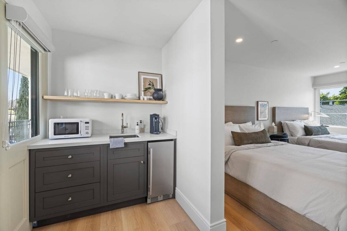 A modern hotel room with a kitchenette, a bed, and a view of the outdoors.