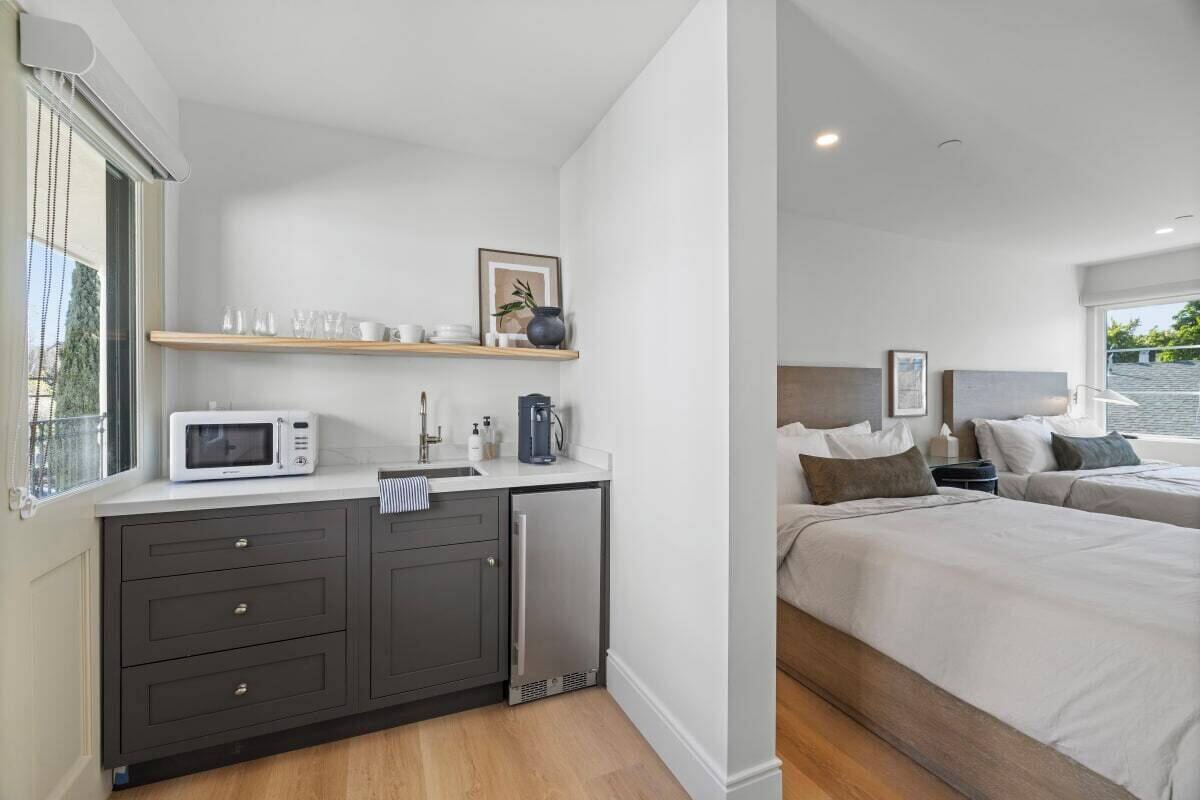A modern hotel room with a kitchenette, a bed, and a view of the outdoors.