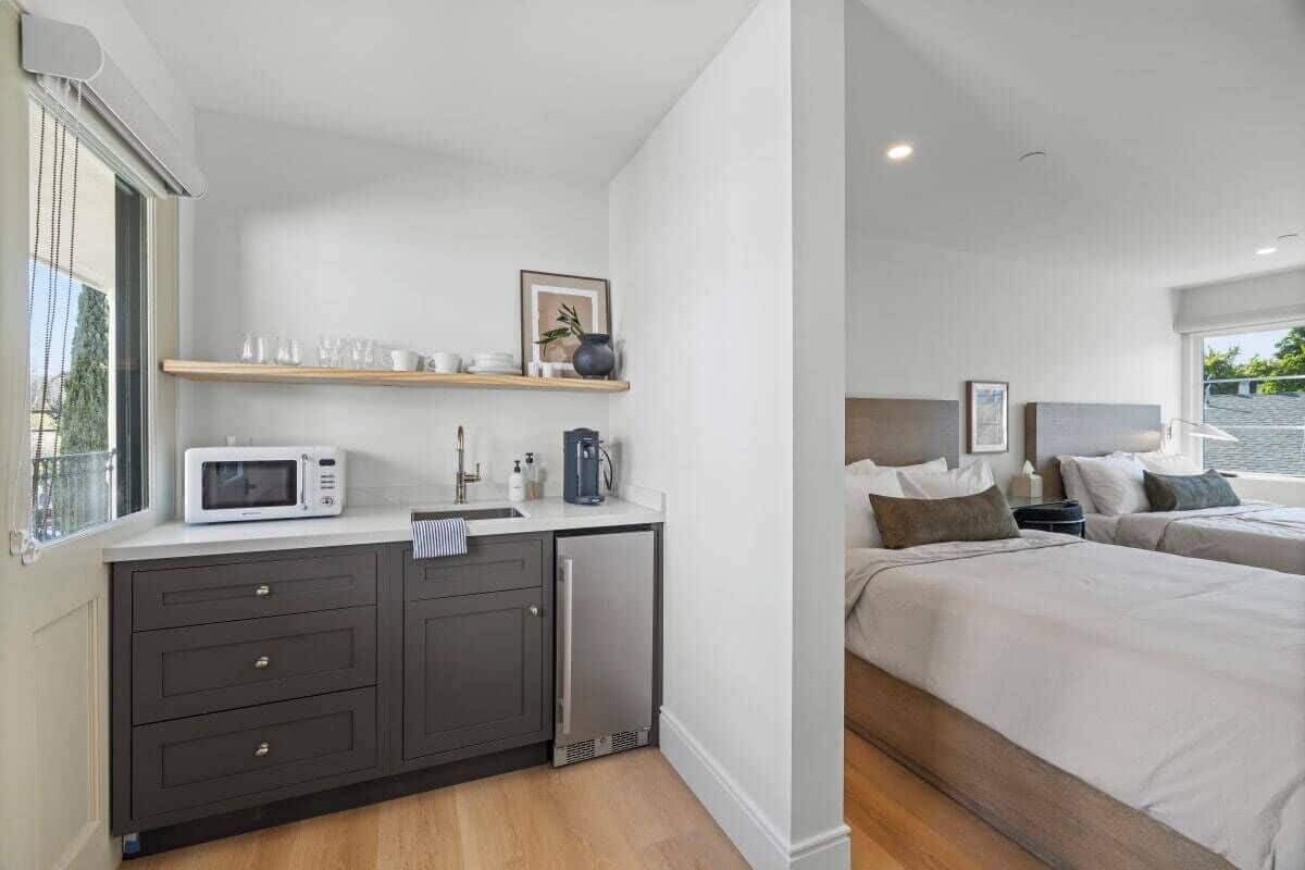 A modern hotel room with a kitchenette, a bed, and a view of the outdoors.