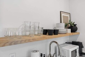 A kitchen with a wooden shelf holding glassware and a white microwave. - Casa Jardin, a ZenStay Hotel (Santa Barbara)