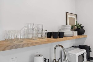 Uma cozinha com uma estante de madeira com copos e um micro-ondas branco.