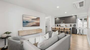 Una sala moderna con un sofá gris, un comedor con mesa y sillas, y una cocina con gabinetes grises y un microondas.