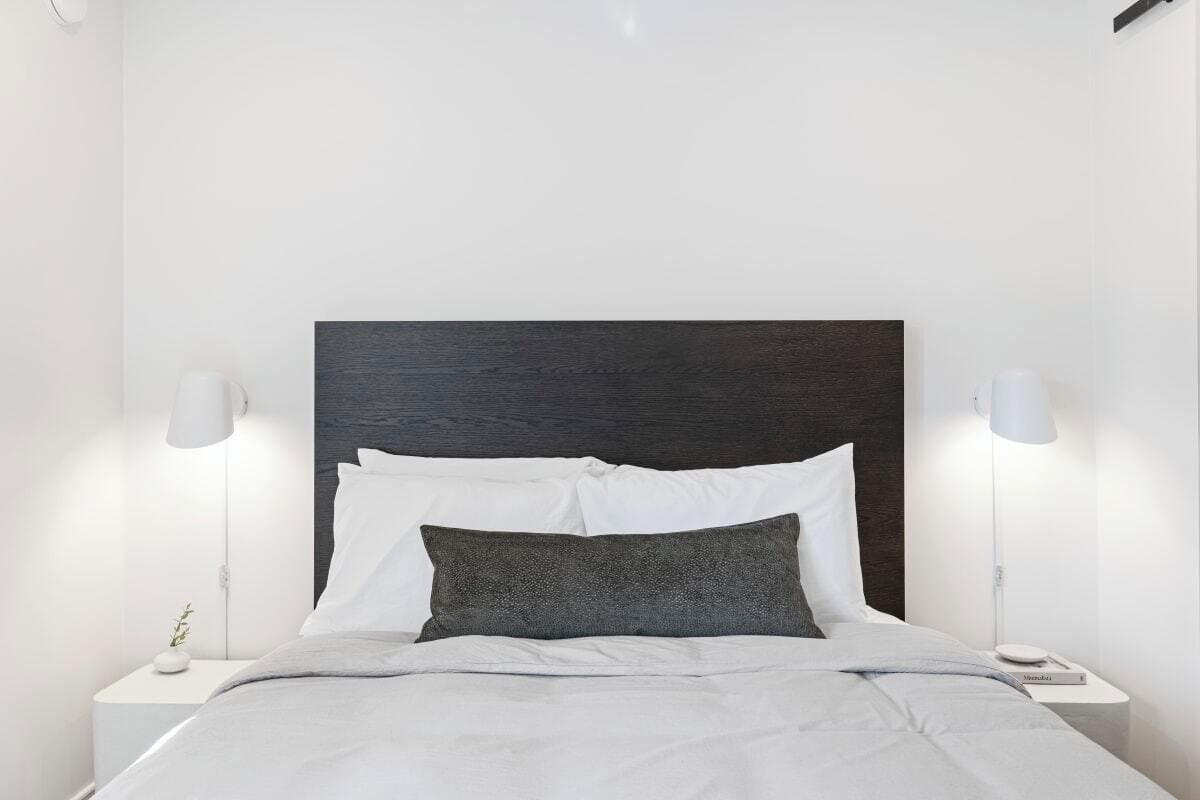 A modern bedroom with a dark wood headboard, white bedding, and bedside lamps.