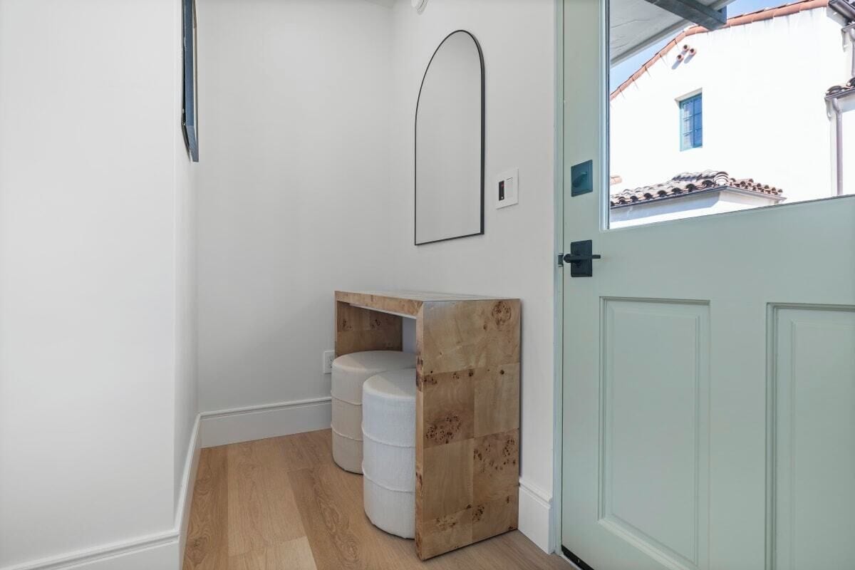 A hallway with a wooden bench, a white door, and a window with a view of a building with a blue window.