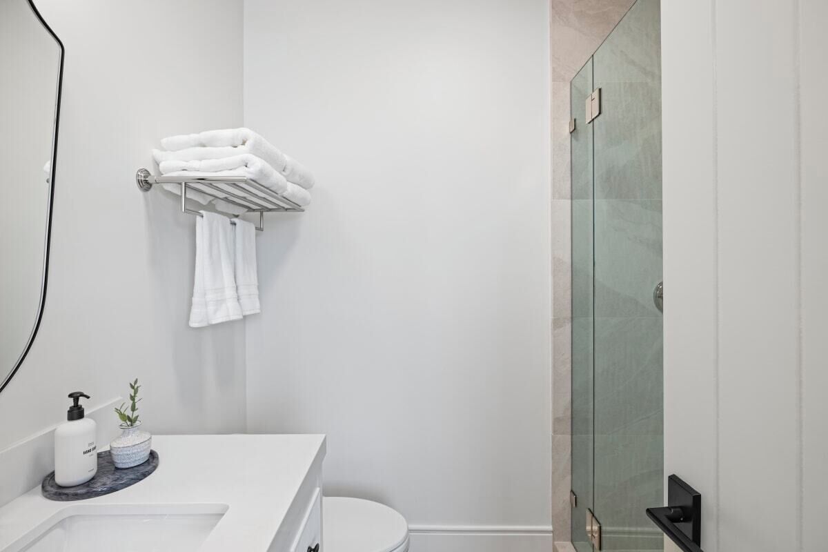 A modern bathroom with a white sink, a glass shower enclosure, and neatly folded towels on a rack.
