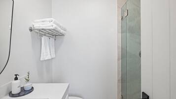 A modern bathroom with a white sink, a glass shower enclosure, and neatly folded towels on a rack.