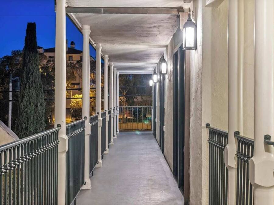 A covered corridor with a railing, columns, and lights.