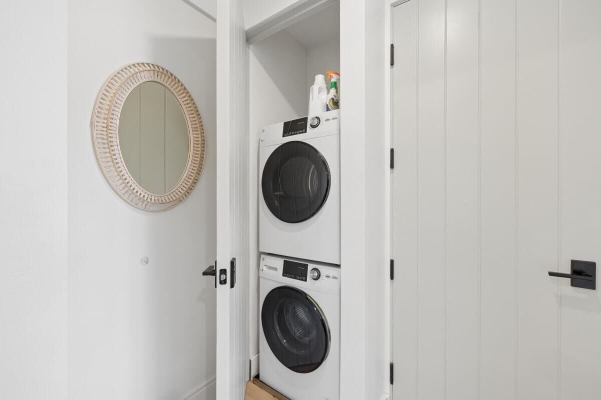 A laundry room with two stacked washing machines and a mirror on the wall.
