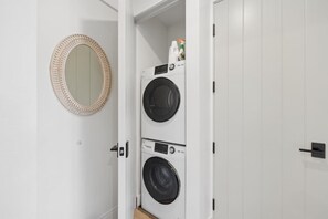 A laundry room with two stacked washing machines and a mirror on the wall. - Casa Jardin, a ZenStay Hotel (Santa Barbara)