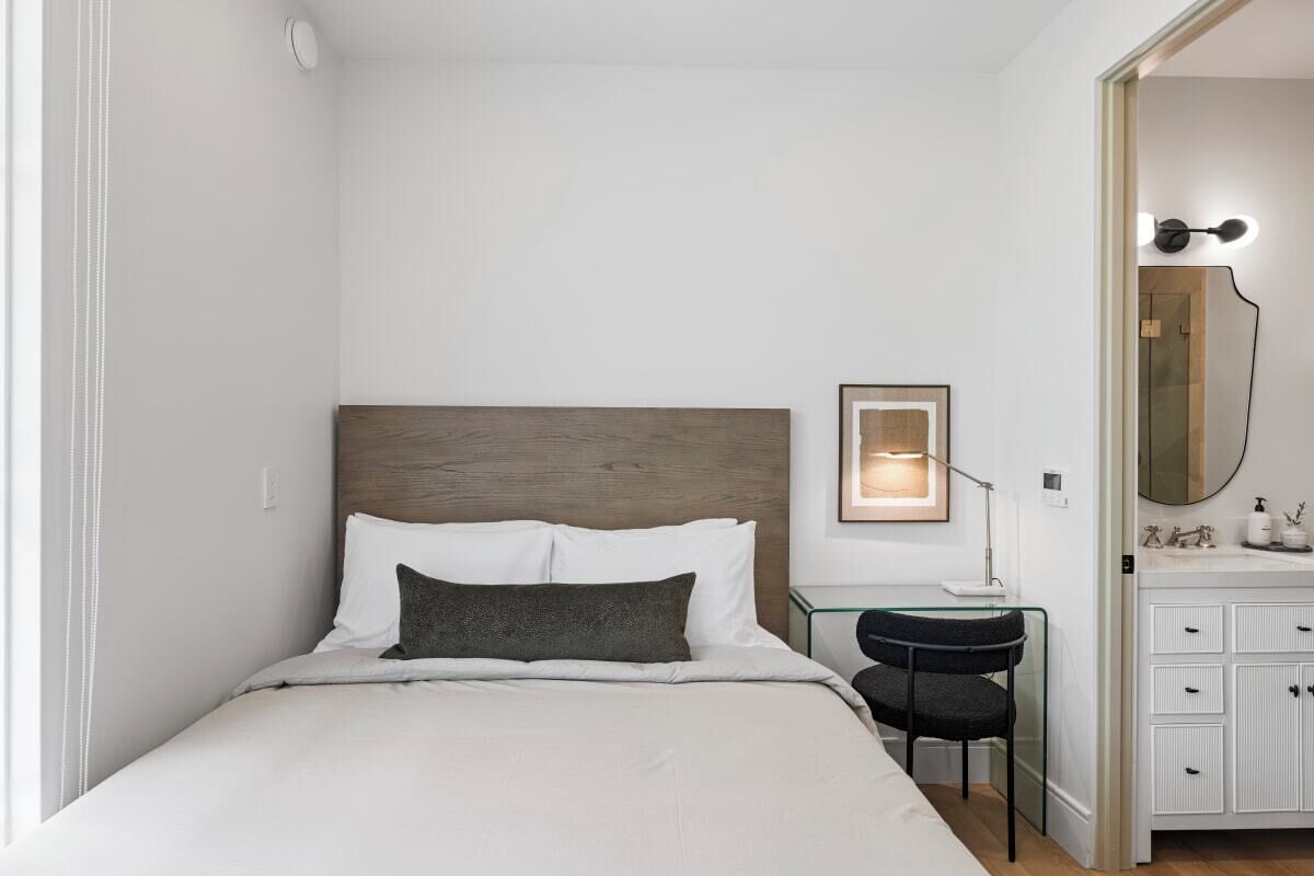 Habitación de hotel ordenada con cama, escritorio, silla y baño con espejo y lavamanos.