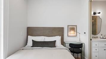 Habitación de hotel ordenada con cama, escritorio, silla y baño con espejo y lavamanos.