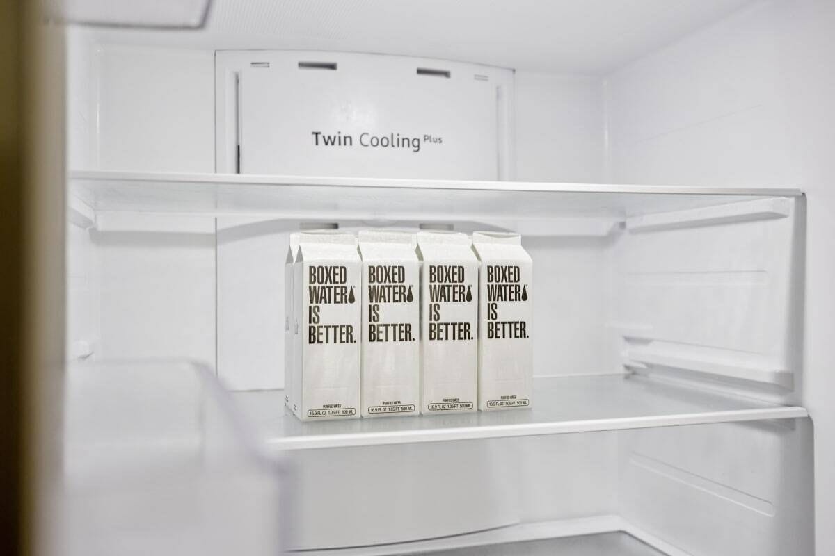 An empty refrigerator with a 'Twin Cooling Plus' label and four cartons of boxed water.
