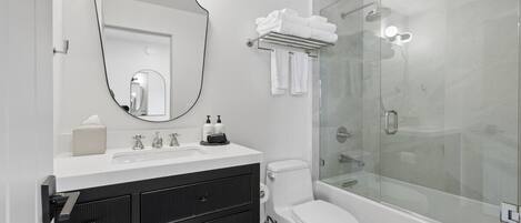A modern bathroom with a glass-enclosed shower, a white sink with a mirror above it, and a black vanity with cabinets.