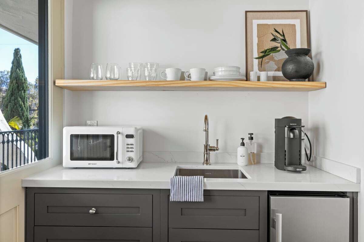 A modern kitchen with a white countertop, a microwave, a coffee machine, and a sink.