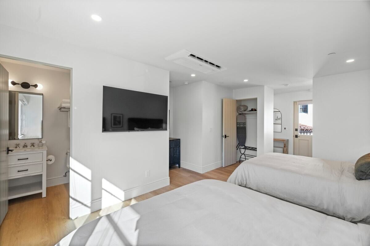 A modern bedroom with two beds, a large mirror, and a TV mounted on the wall.