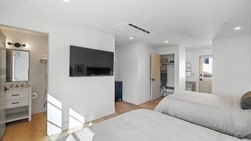 A modern bedroom with two beds, a large mirror, and a TV mounted on the wall.