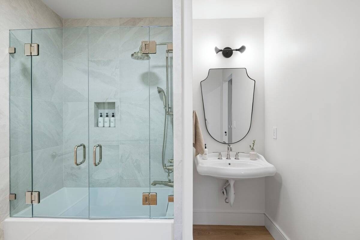 A modern bathroom with a glass-enclosed shower, a white sink, and a large mirror.