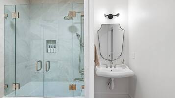 A modern bathroom with a glass-enclosed shower, a white sink, and a large mirror.