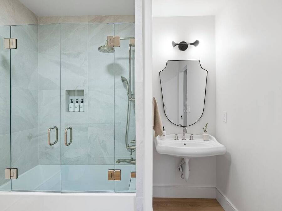 A modern bathroom with a glass-enclosed shower, a white sink, and a large mirror.