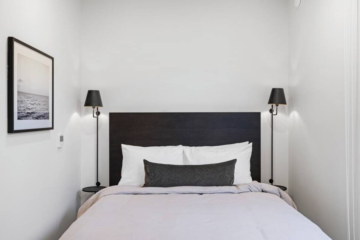 A neatly made bed with white and grey bedding, two black lamps on either side, and a framed picture on the wall.