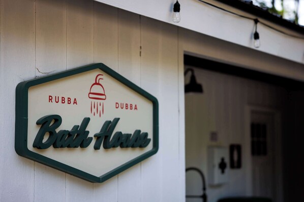 A sign for 'Bath House' with a bell icon and the words 'RUBBA DUBBA' on a white wall.