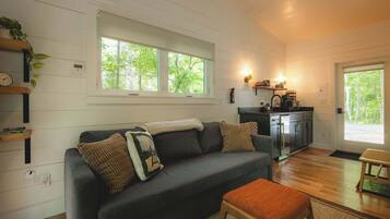 A cozy living room with a dark grey sofa, a wooden bench, and a kitchen area with cabinets and a countertop.