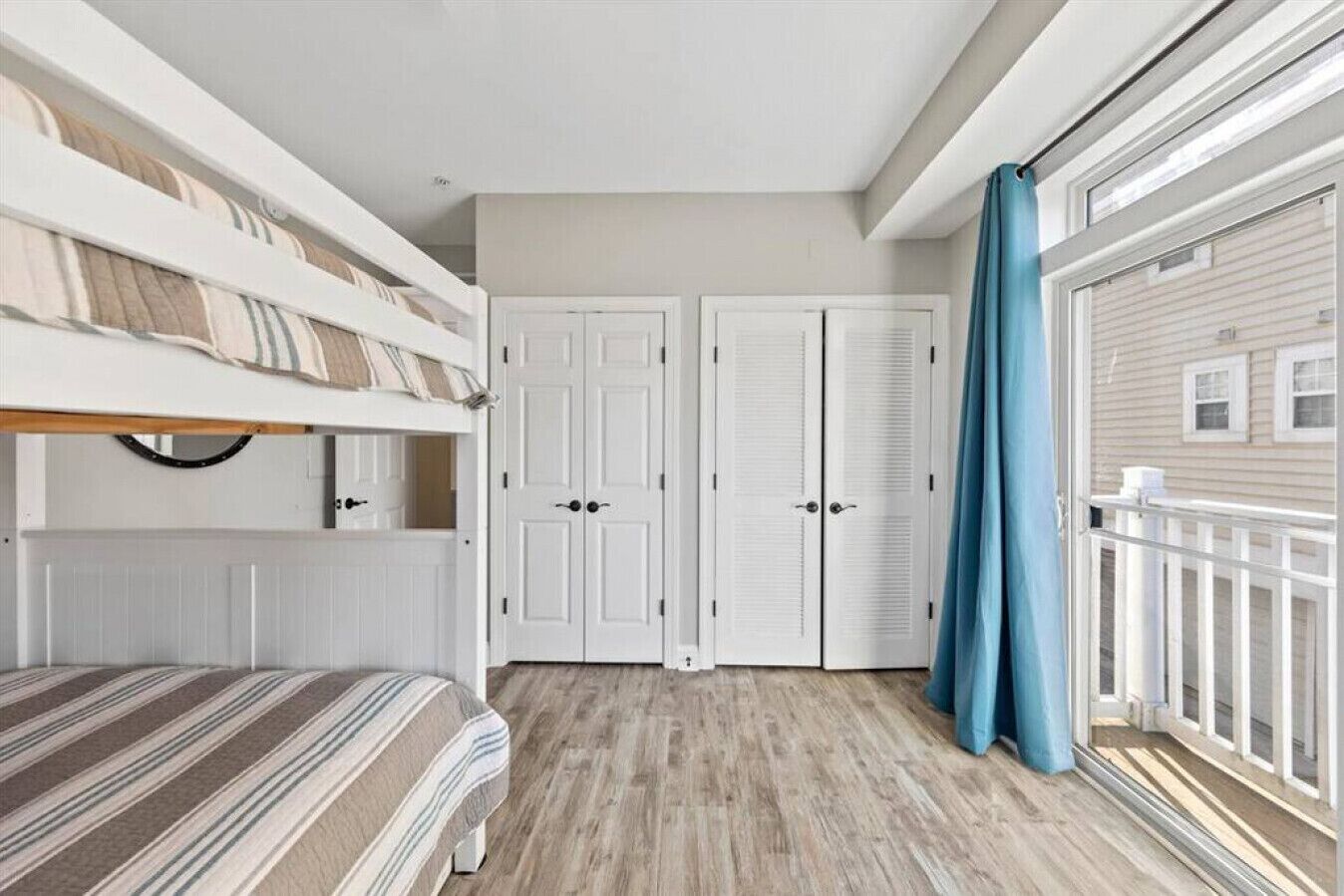 Un dormitorio con una cama individual superpuesta, un armario y un balcón con cortinas.