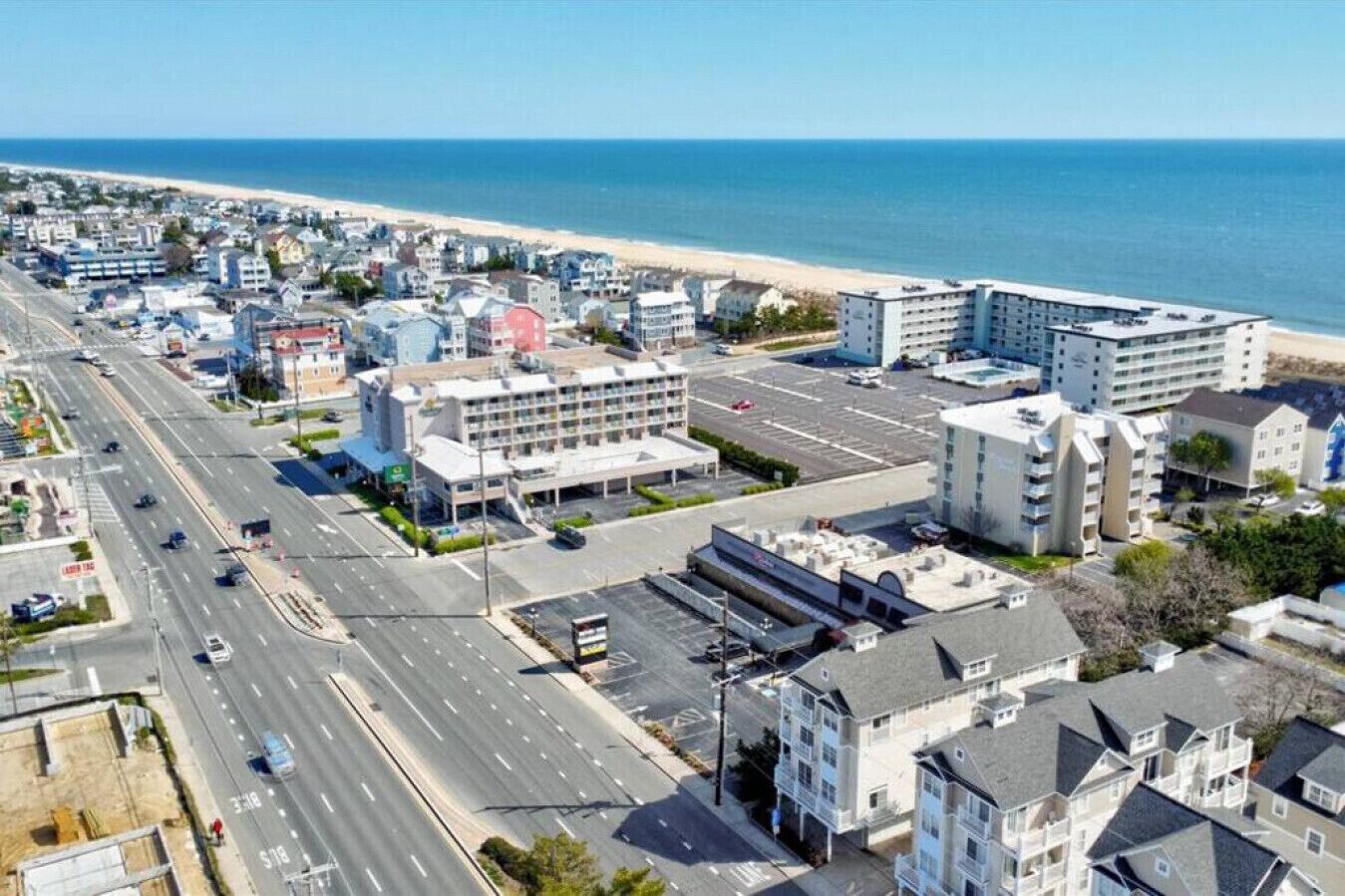 A coastal cityscape with a wide road, beachfront buildings, and a large hotel with multiple floors and balconies.